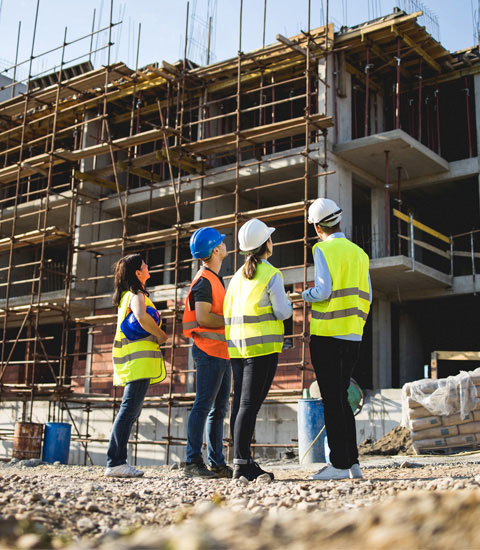 Construction workers in safety gear inspecting a commercial building site with scaffolding — workplace safety and construction project management