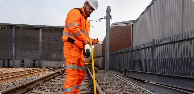 Worker wearing high‑visibility protective clothing using equipment on railway tracks
