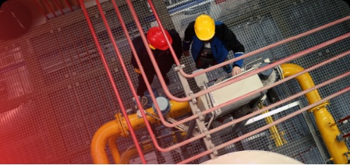 Two workers wearing protective helmets and safety gear operating within an industrial facility, viewed from above