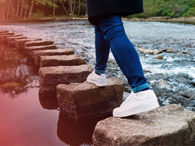 Person stepping across large stones over a stream