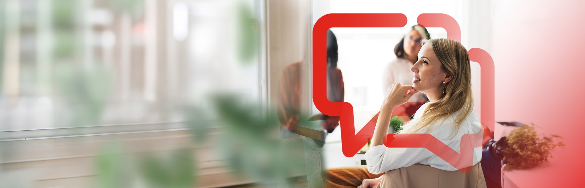 People collaborating in a modern office meeting area, with one person seated in the foreground and others talking nearby