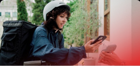 A delivery rider sitting on a bike in an outdoor urban setting, holding a smartphone